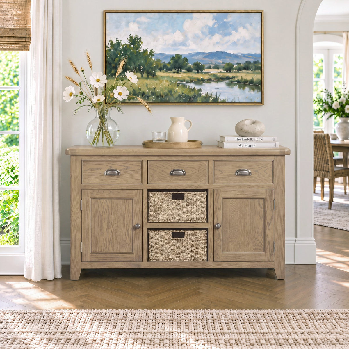 A light natural wood sideboard cabinet with three drawers, two cabinet doors, and two woven storage baskets, styled in a bright, modern living room setting.