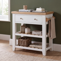 A white kitchen utility cart with a light wood top, two drawers, two open shelves, and a towel rack on the side, styled in a kitchen setting.