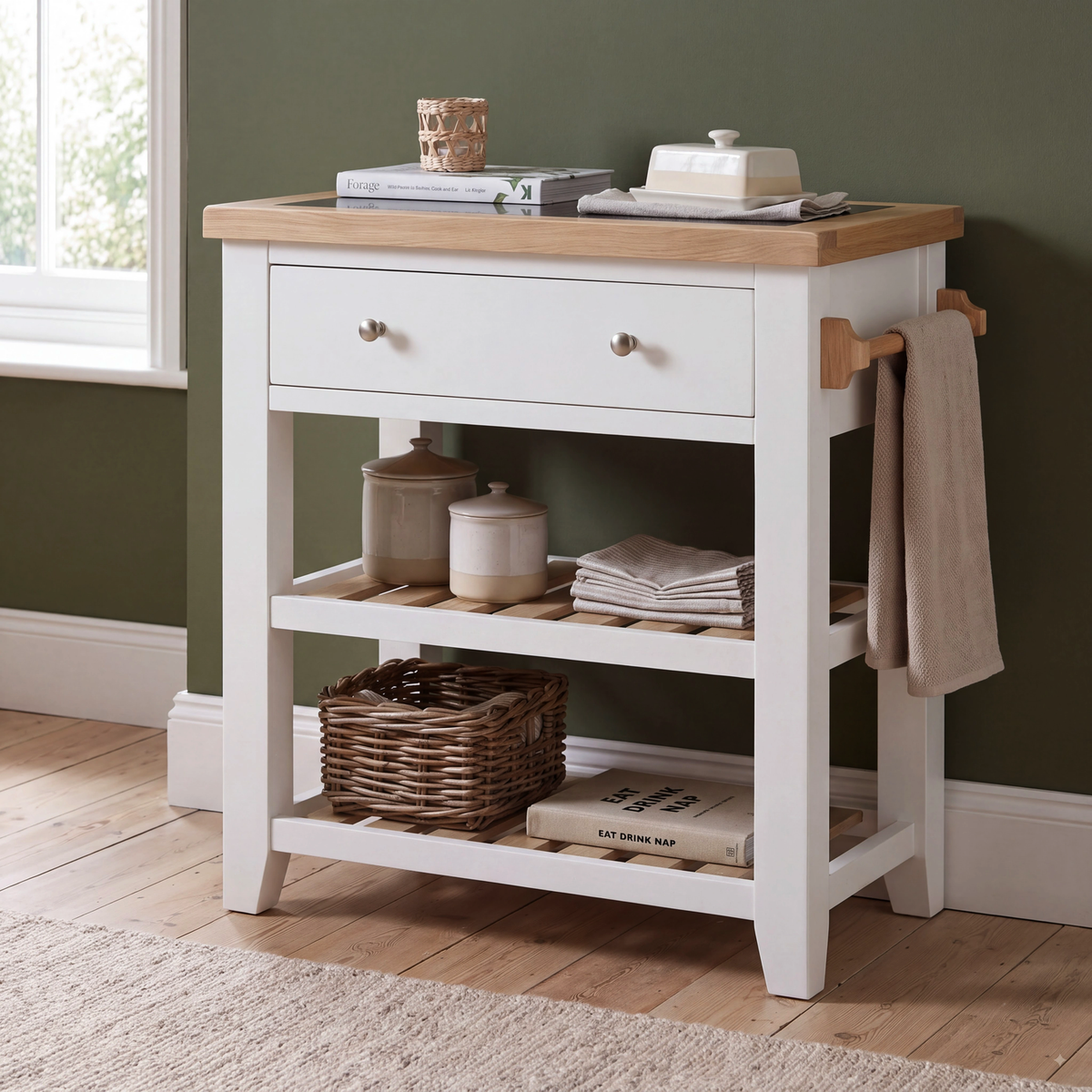 A white kitchen utility cart with a light wood top, two drawers, two open shelves, and a towel rack on the side, styled in a kitchen setting.