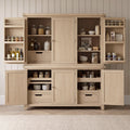 A large light oak kitchen pantry cabinet with multiple doors and open shelves, styled with glass jars, bottles, bowls, and utensils, set against a paneled wall and wood floor.