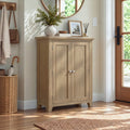 A light oak wood entryway cabinet with two doors and silver knobs, styled in a bright entryway with a plant, picture frame, and a wicker basket nearby.