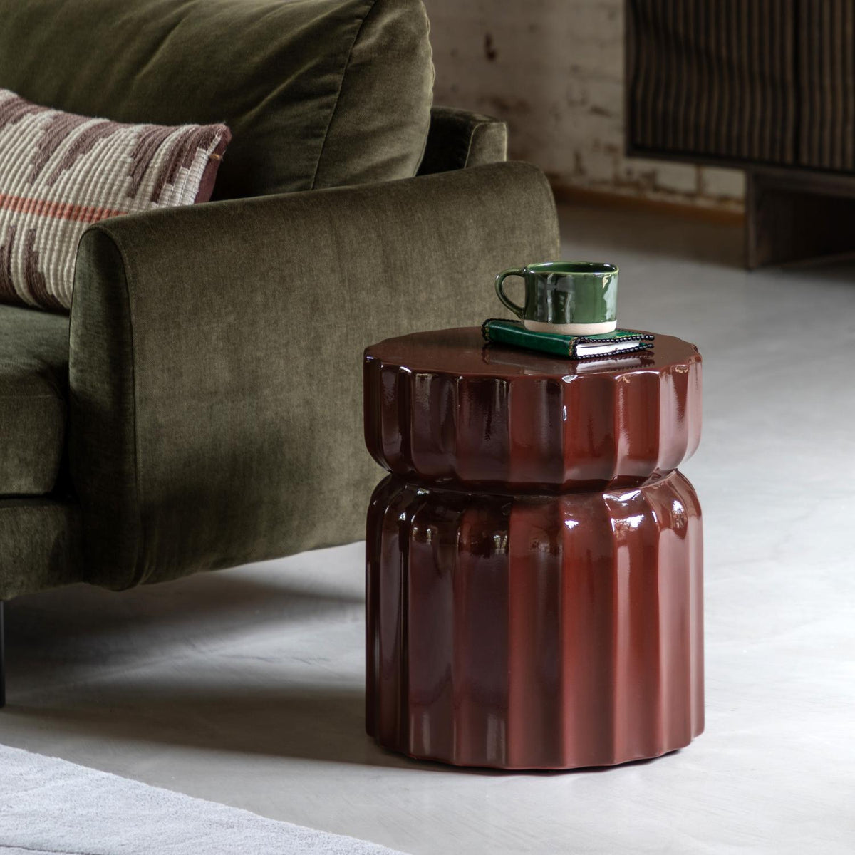 Brown textured side table with a green mug and book in a living room setting.