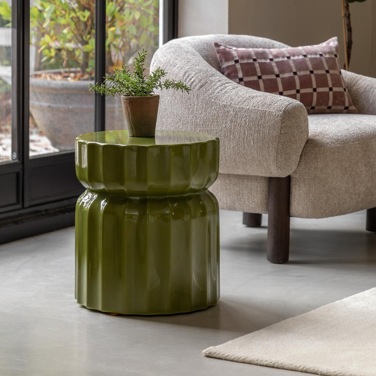Green side table in a living room setting with a plant and armchair.