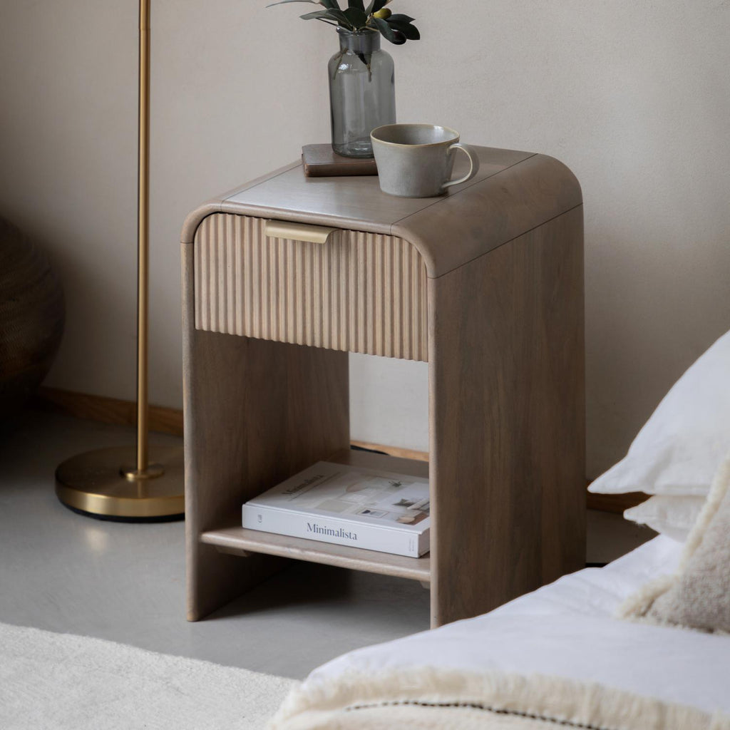 Wooden nightstand with a cup, book, and vase in a bedroom setting