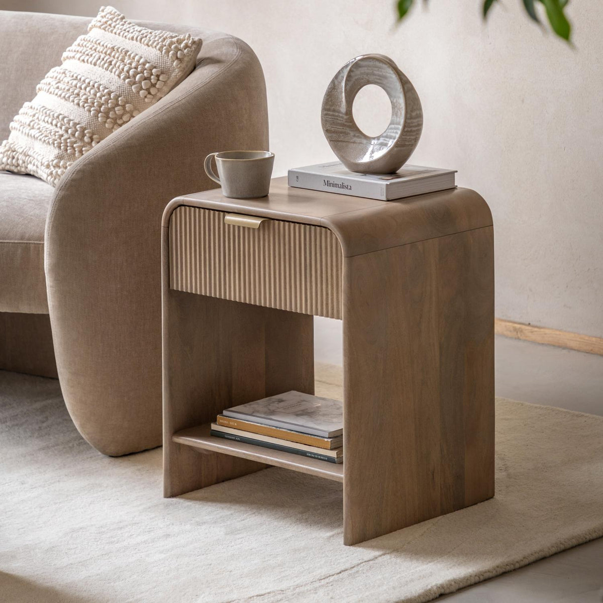 Wooden side table with a cup, books, and decorative object in a living room setting.