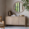 Wooden sideboard with decorative items in a room with a round mirror and plant.