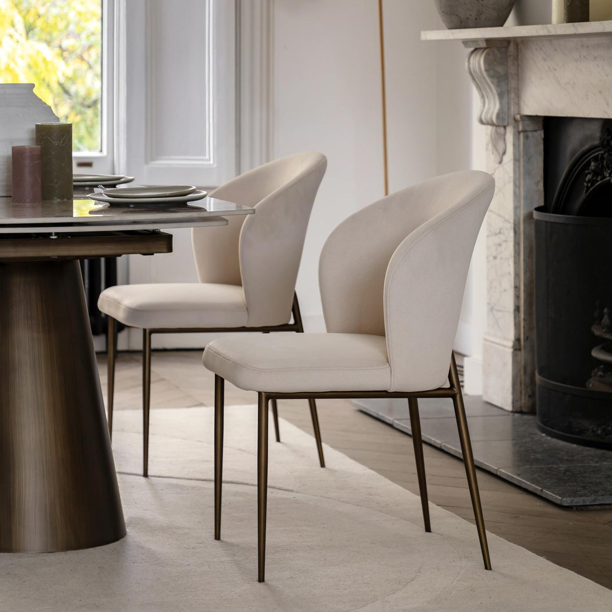 Dining room with a table and two beige chairs in front of a fireplace.