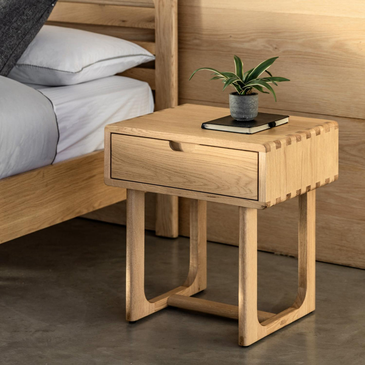 Wooden bedside table with a plant and book next to a bed