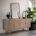 Wooden sideboard with a mirror and decorative items in a room with a plant.