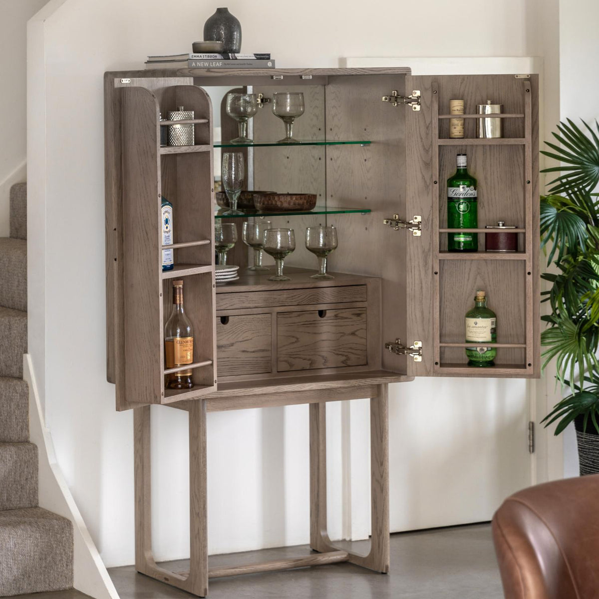 Wooden bar cabinet with open doors displaying bottles and glasses in a home setting.