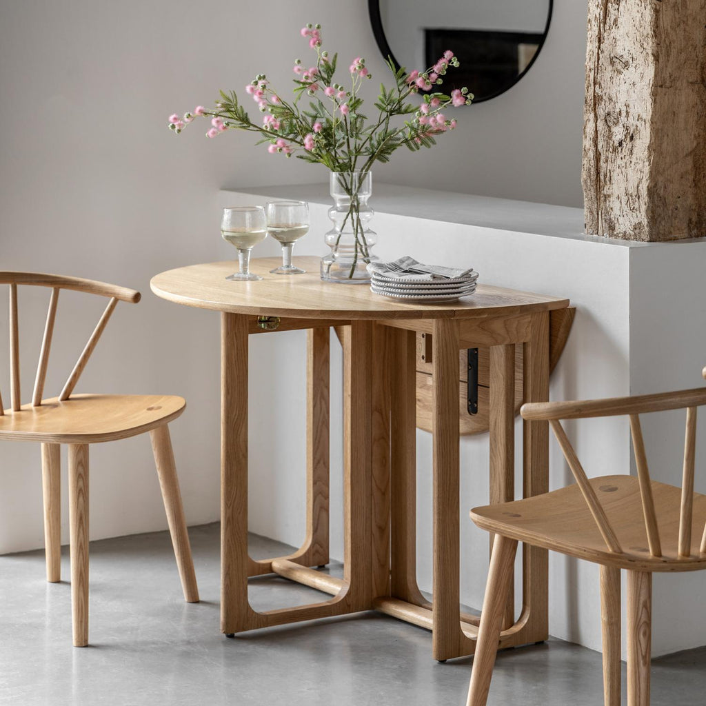 Wooden dining table with chairs and a vase of flowers in a minimalistic setting.