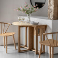 Wooden dining table with chairs and a vase of flowers in a minimalistic setting.