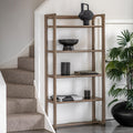 A tall, five-tier wooden shelving unit with a weathered brown finish, styled with home decor items next to a staircase and a potted plant.