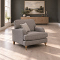 A light gray upholstered armchair with turned wooden legs and a striped throw pillow, placed in a styled living room with dark gray walls, a wood console, and a landscape painting.