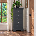 A tall, narrow dark charcoal gray chest of drawers with five drawers and silver knobs, styled in a bright room next to a window and wooden door.