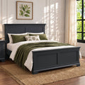 A dark charcoal gray wooden bed frame with a tall headboard and footboard, styled with white bedding, olive green pillows, and a green throw blanket, set on a natural jute rug in a bright bedroom.