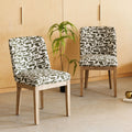 Two upholstered dining chairs with a black and white abstract brushstroke pattern and light natural wood legs, set in a room with a light wood paneled wall and concrete floor.