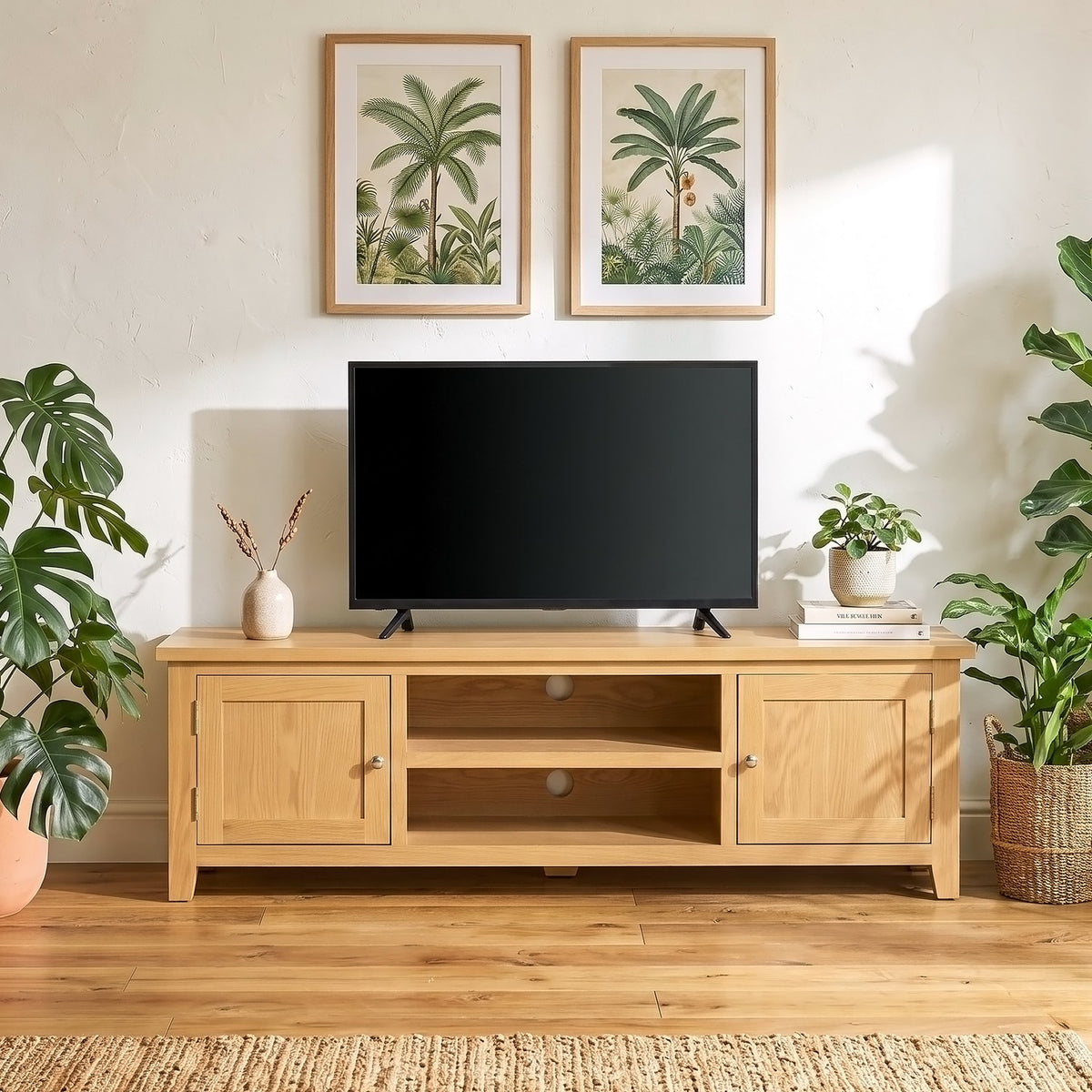 A light natural wood TV stand with cabinet doors and open shelving, styled in a living room setting with a black flat-screen TV on top, framed botanical prints on the wall, and potted plants on both sides.