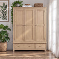 A tall light oak wood three-door armoire cabinet with a drawer base, styled in a bright room with plants, books, and a basket on top.