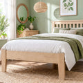 A light natural wood bed frame with a slatted headboard and footboard, styled with white bedding and a textured green throw blanket in a bright, modern bedroom.