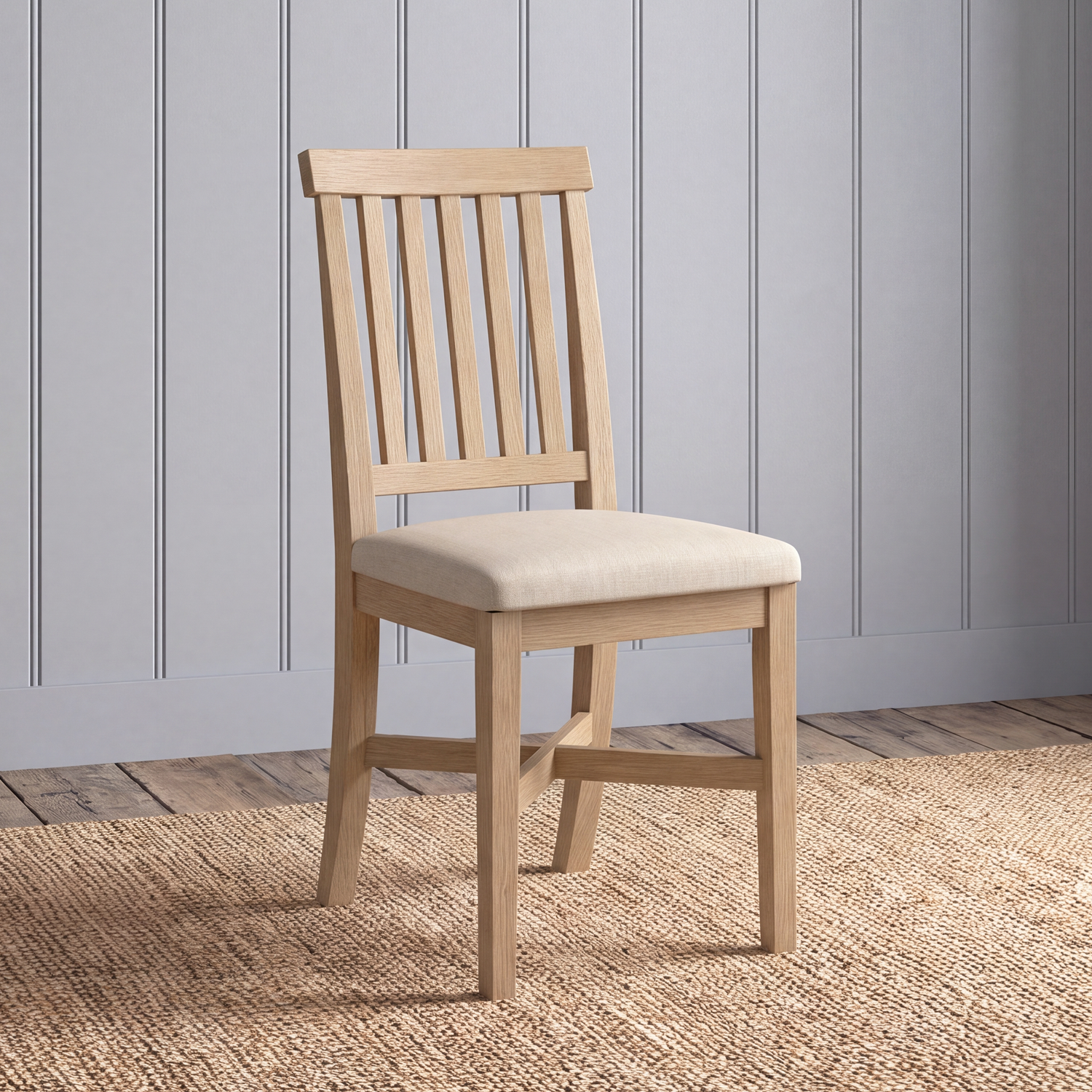 A light natural wood dining chair with a slatted backrest and a cream upholstered seat, shown standing on a woven jute rug against a gray paneled wall.