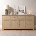 A light oak wood sideboard cabinet with six drawers and four doors, styled with a lamp, vases, a framed print, and candles against a neutral beige wall.