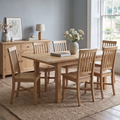 A light natural oak dining set consisting of a rectangular table and six matching slatted-back chairs, styled in a bright dining room next to a matching wooden sideboard.