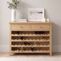 A light natural wood wine cabinet with two drawers and four wine bottle racks, styled with a vase, books, and a framed print on a neutral wall.