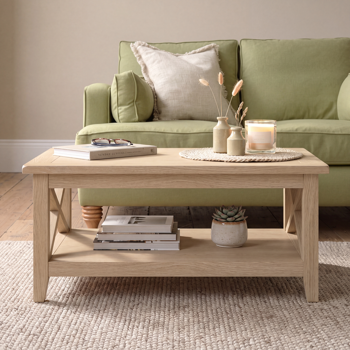A light natural wood coffee table with an open lower shelf, styled in a living room setting with a green sofa, books, and decorative vases in the background.