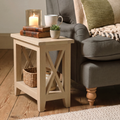 A light natural wood end table styled in a cozy living room next to a gray armchair, holding a lit candle, books, a white mug, and a small potted succulent.