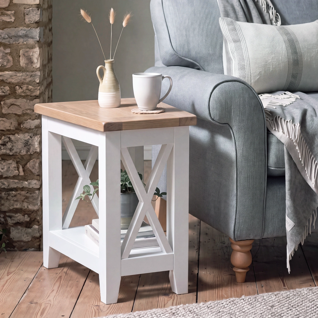 A rustic white wooden end table with a light oak top, styled next to a gray armchair in a cozy living room setting.