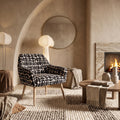 Sloane chair with arms in black and cream geometric pattern boucle style fabric on beech-wrapped metal legs beside a fireplace