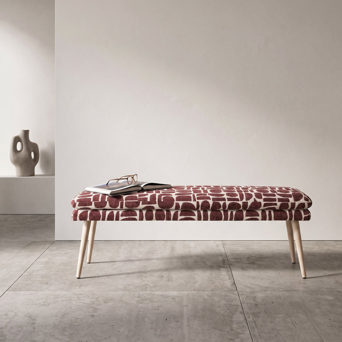 Sloane 140cm flat bench in plum geometric pattern boucle style fabric with a book and glasses on a stone floor